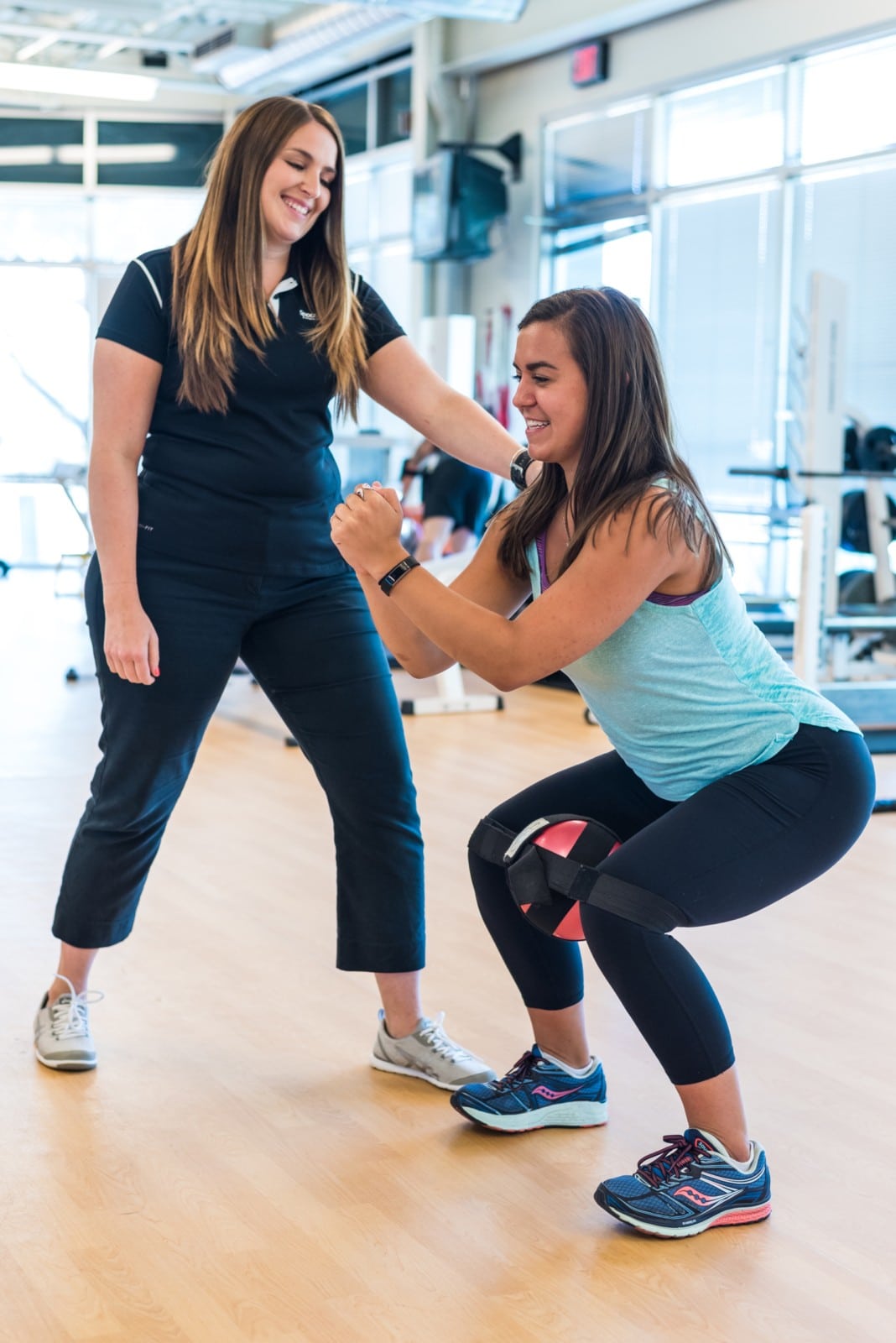 A woman squatting while holding a medicine ball in between her knees.