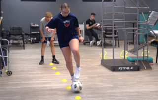 A young athlete kick a soccer ball around yellow cones.