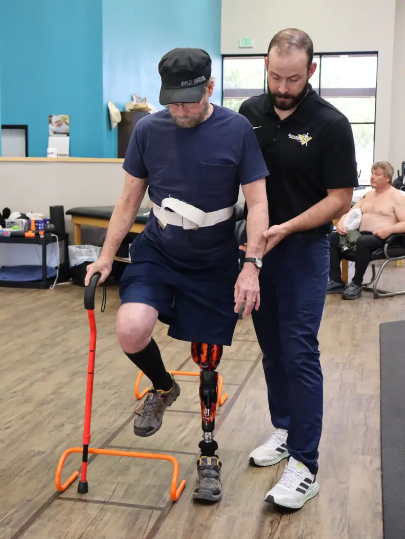 Image of a therapist helping a man with a prosthetic leg get used to the feel of it.