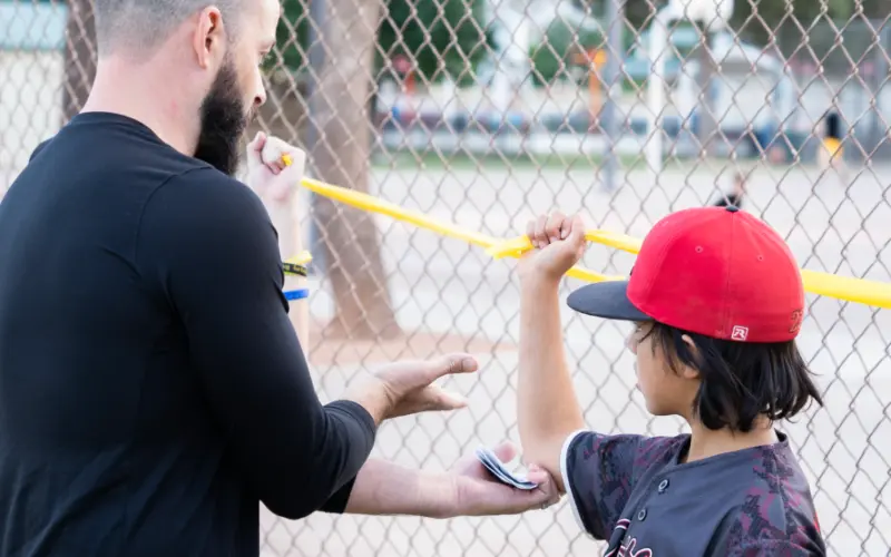 A young boy exercises his shoulder with a yellow elastic band.