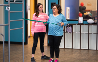 A breast cancer rehabilitation patient in a blue shirt doing pull backs with a resistance band.