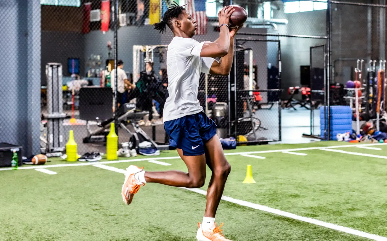 A college football player catching a football on an indoor green.