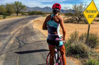 A female cyclist on a road in the desert.