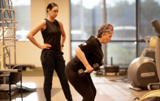 A breast cancer survivor doing bent over rows with dumbbells as Andrea Renteria, PT, DPT monitors her form.