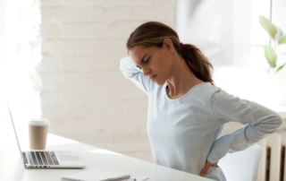 Woman sitting in front of her laptop and messaging her neck.