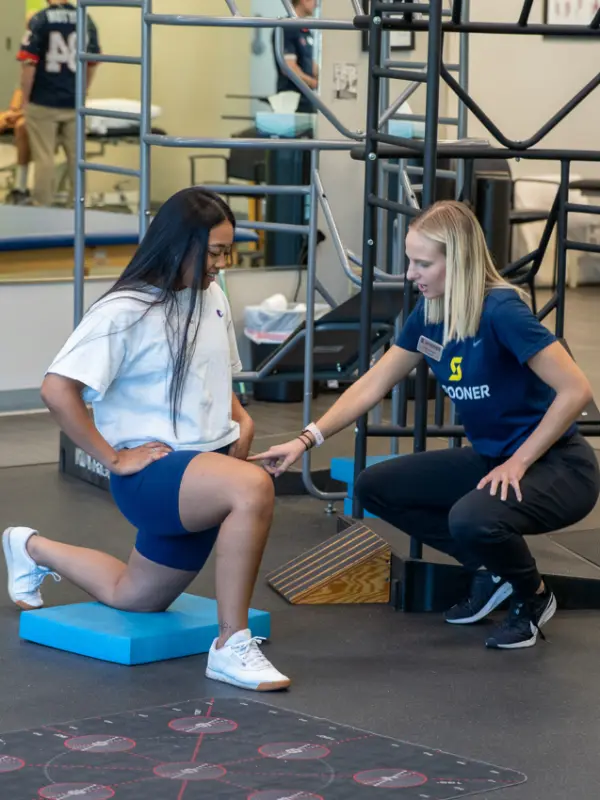 Image of a FIT trainer helping a woman do kneeling lunges.