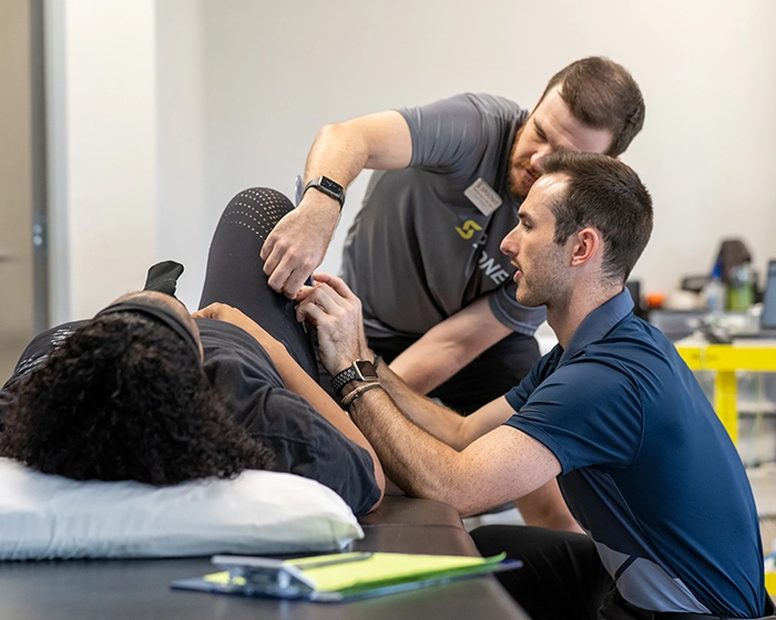 A physical therapist and a physical therapy tech work on the leg of a woman laying on a table.