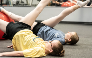 Two dancers lifting their legs in the air during an exercise routine.