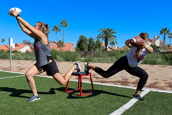 Two woman doing single leg elevated lunges.