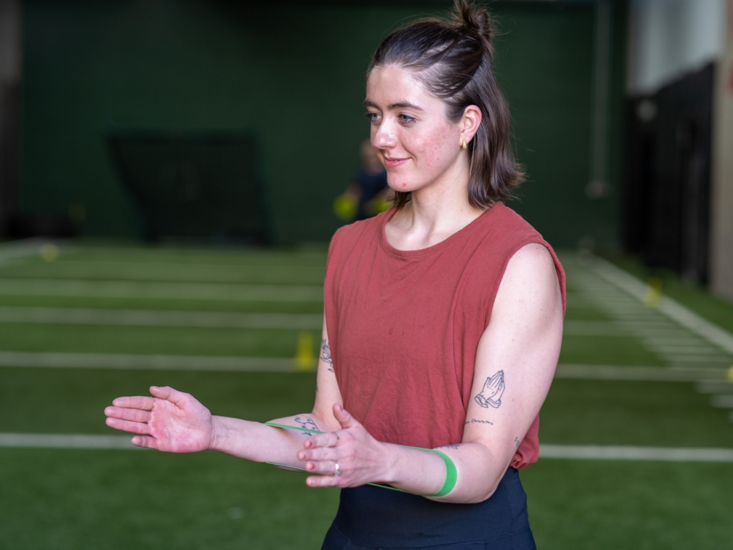 Woman with a tension band around her forearm, elbows bent at 90 degrees, in the banded external rotation starting position.