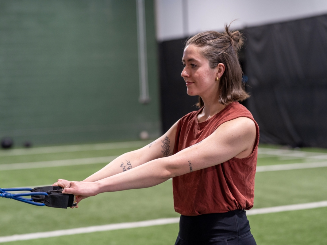 Image of a woman doing the face pull exercise in the starting position with her arms out stretched holding on to a tension rope.