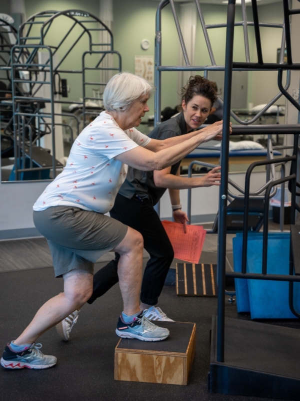 Image of Carrie Yaeger next to an elderly female patient stepping up on a wooden platform.