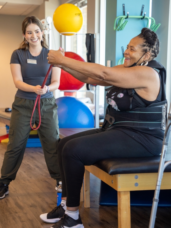 Image of a woman in a back brace sitting on a table with her arms outstretched forward.