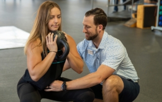 Feature image of a woman holding a kettlebell as she squats with a physical therapist holding her hip in alignment.