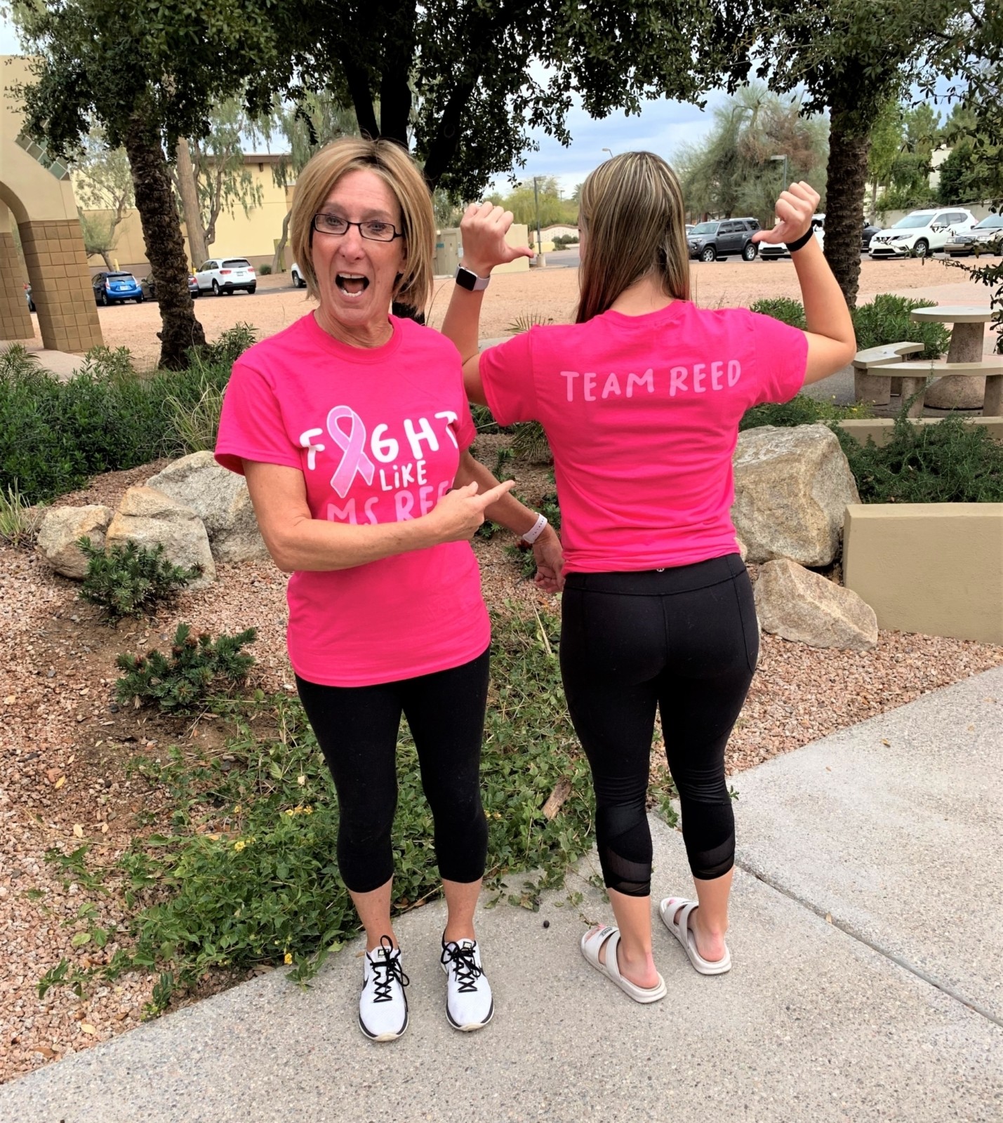 Two women wearing pink shirts as one points to the back of the other.